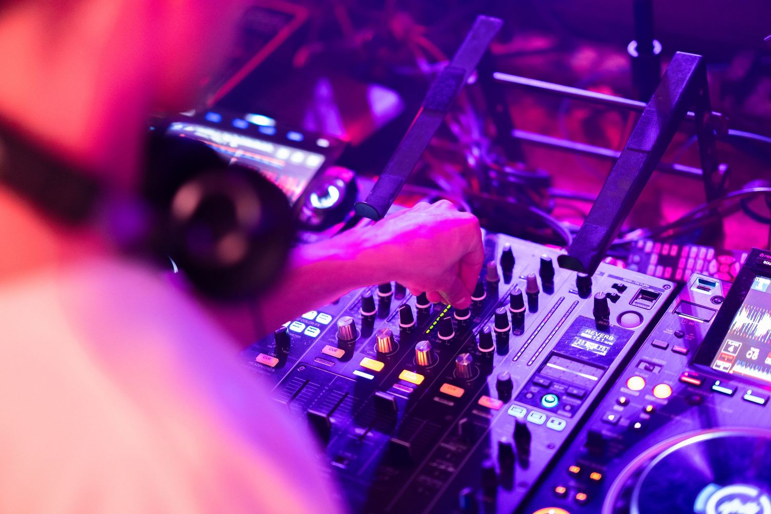 Professional DJ equipment and mixer controls illuminated by vibrant pink and purple lights.