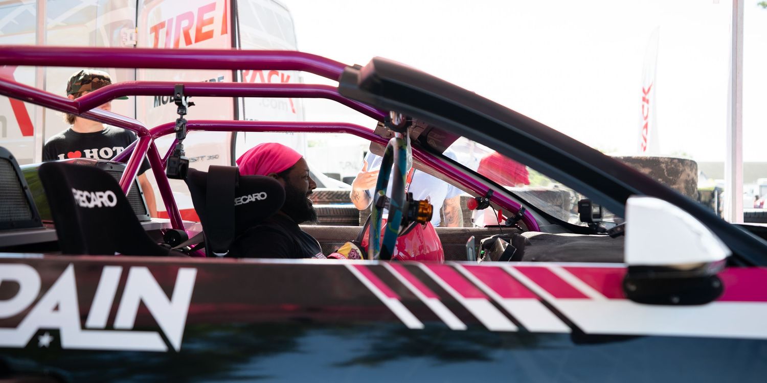Pink and black drift car with roll cage and PAIN livery parked at a motorsport event.