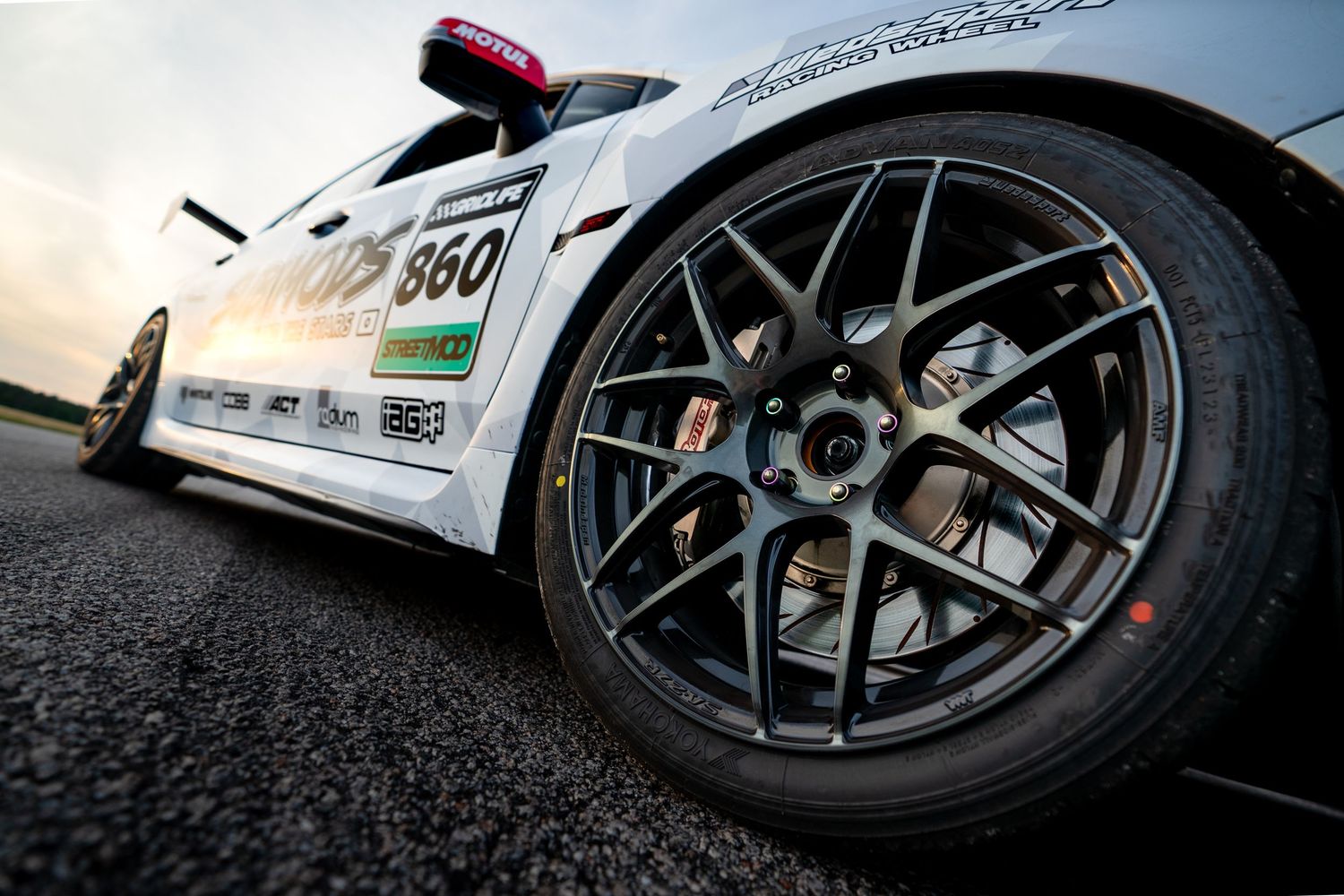 Close-up of a racing car's dark alloy wheel with red brake calipers on a track surface.
