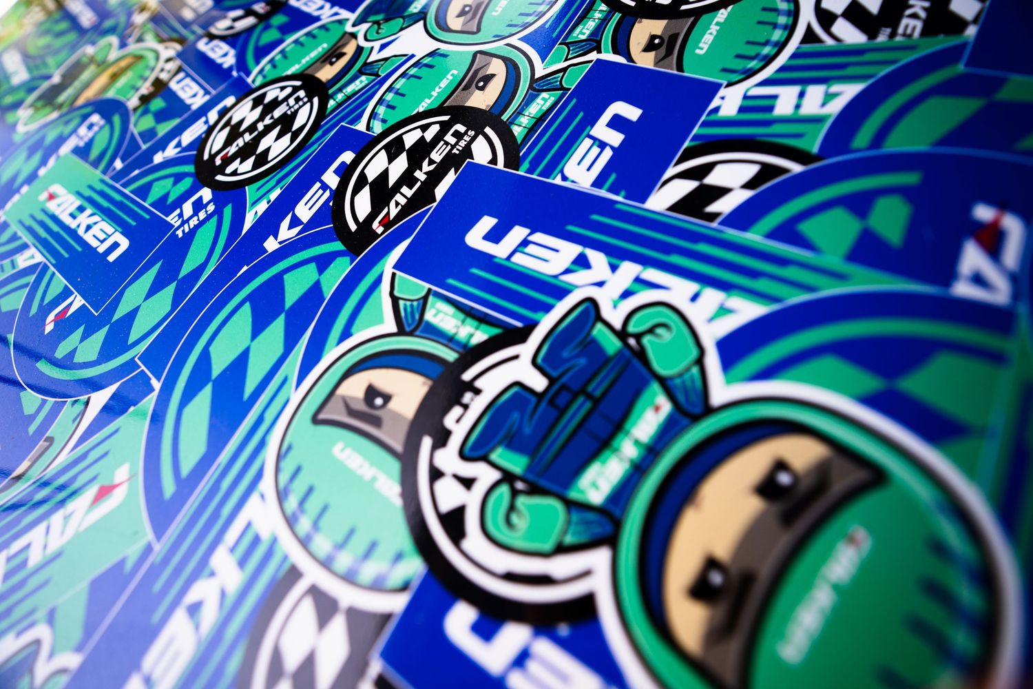 Colorful Falken Tire stickers and decals spread out on a flat surface at a racing event.