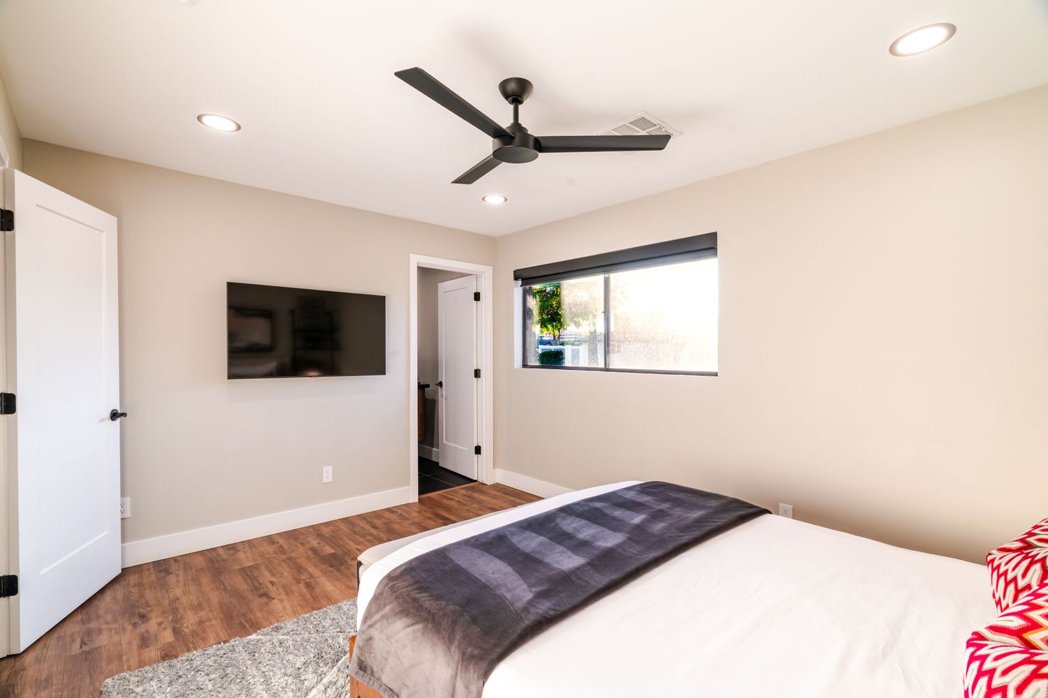 Spacious bedroom with white walls, ceiling fan, and natural light streaming through windows.