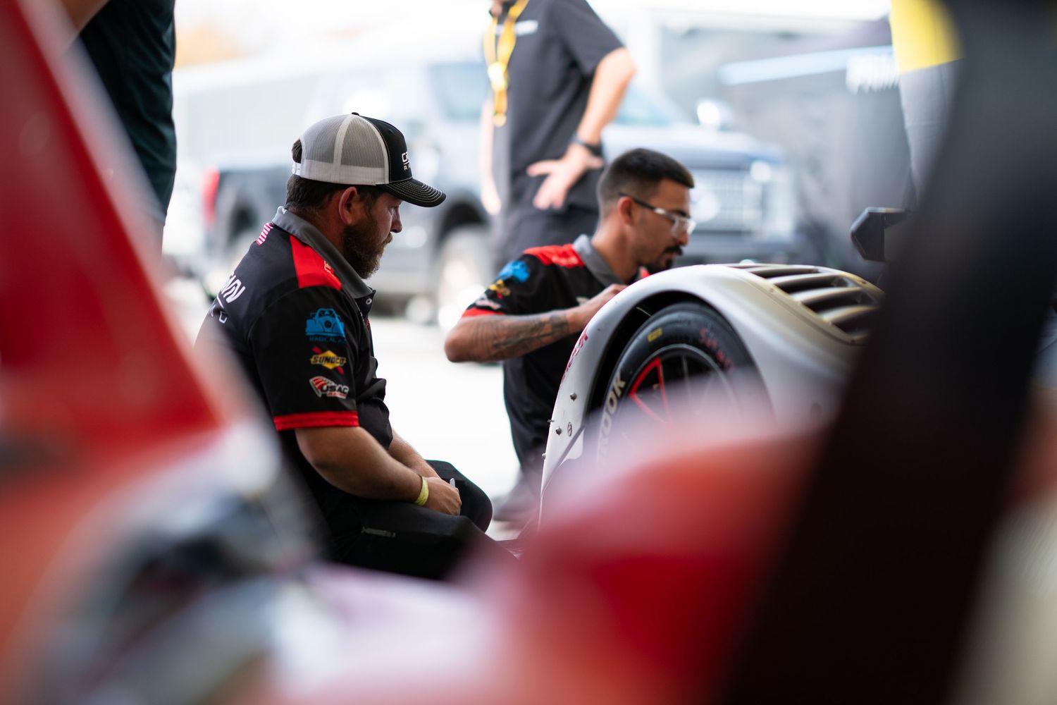 Racing team personnel working together in a pit lane environment.