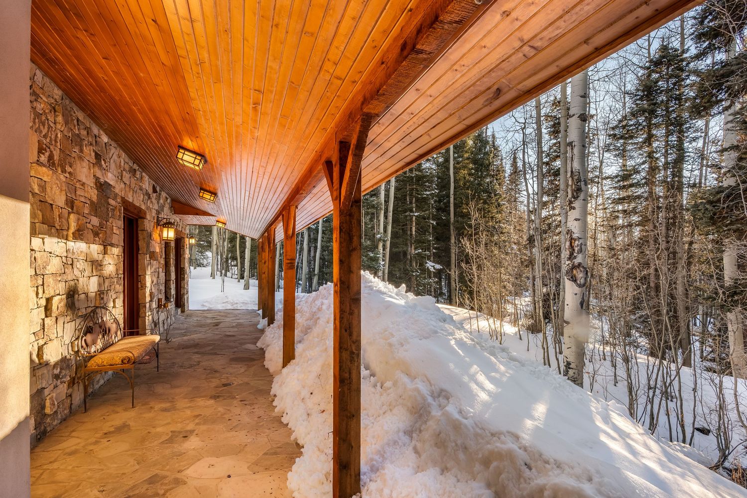 Snow-covered wooden deck with forest views extends around a rustic cabin in winter landscape.