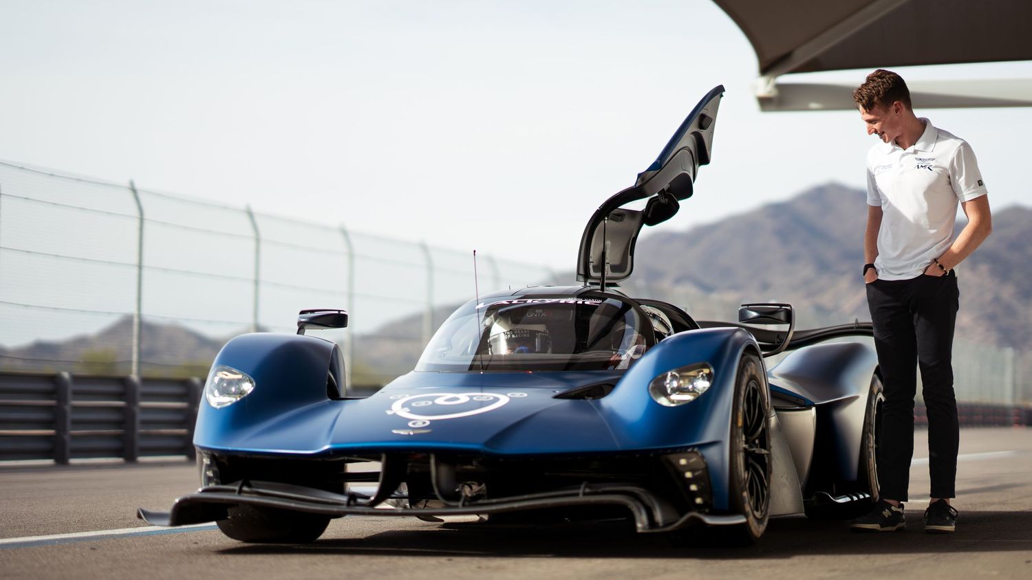 Sleek blue Aston Martin Valkyrie hypercar on display at a race circuit.
