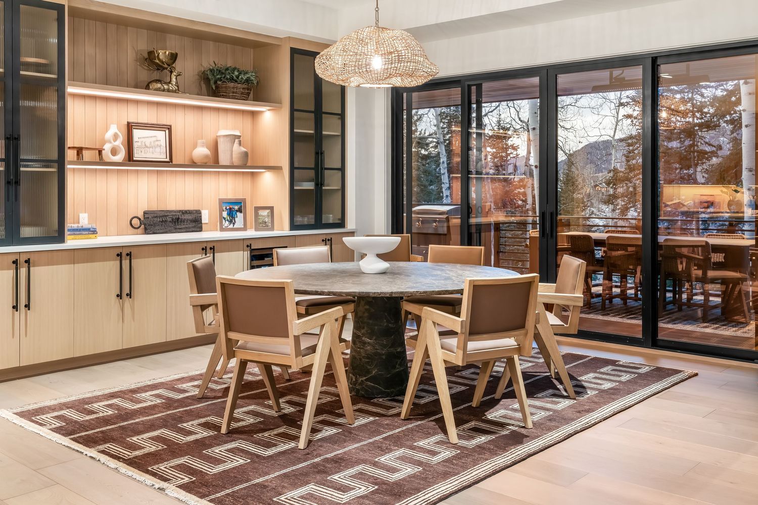 Modern office space with wooden tables, gray carpet, and large windows offering natural light and outdoor views.