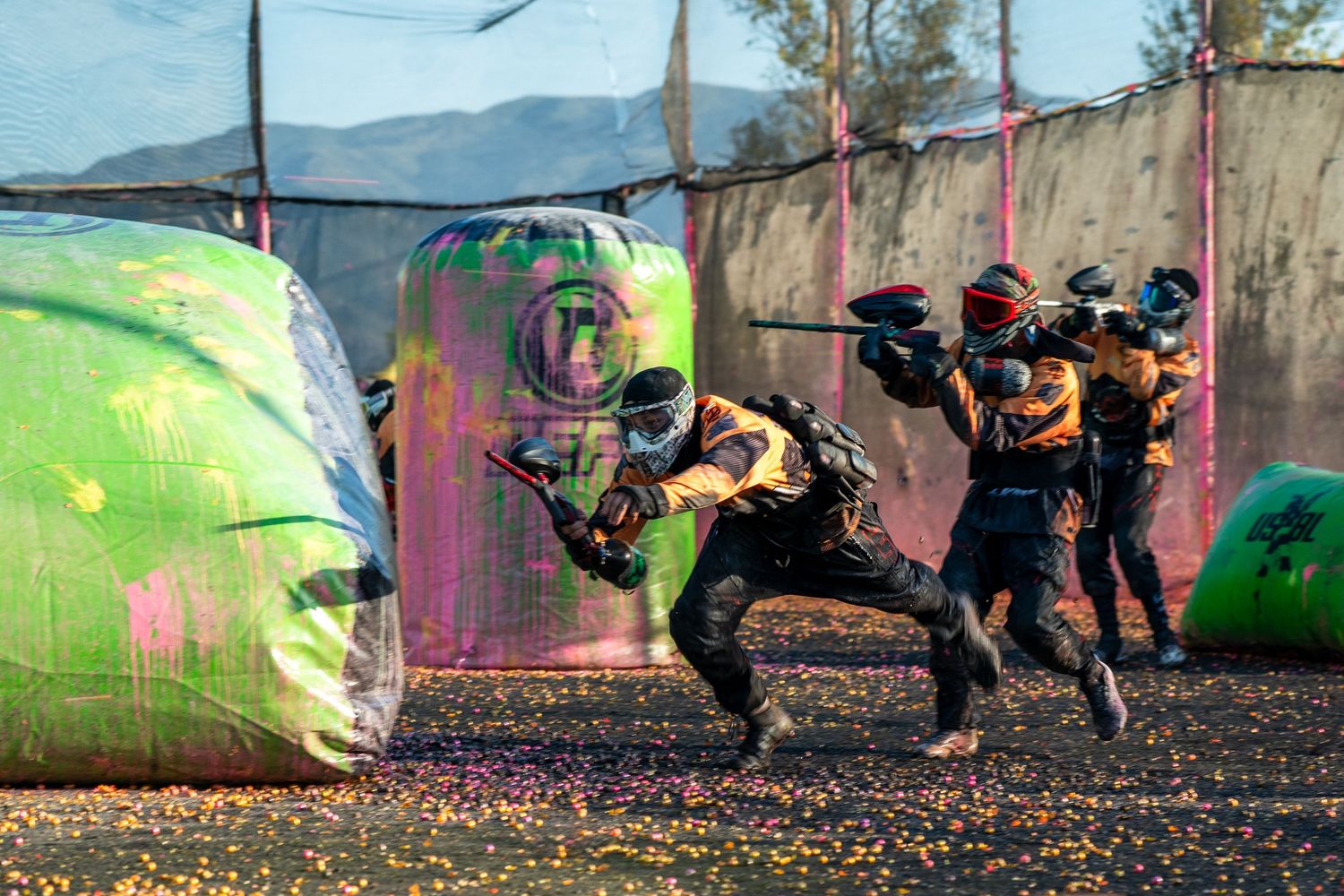 Players in protective gear engage in an intense paintball match on a colorful outdoor field with inflatable bunkers.