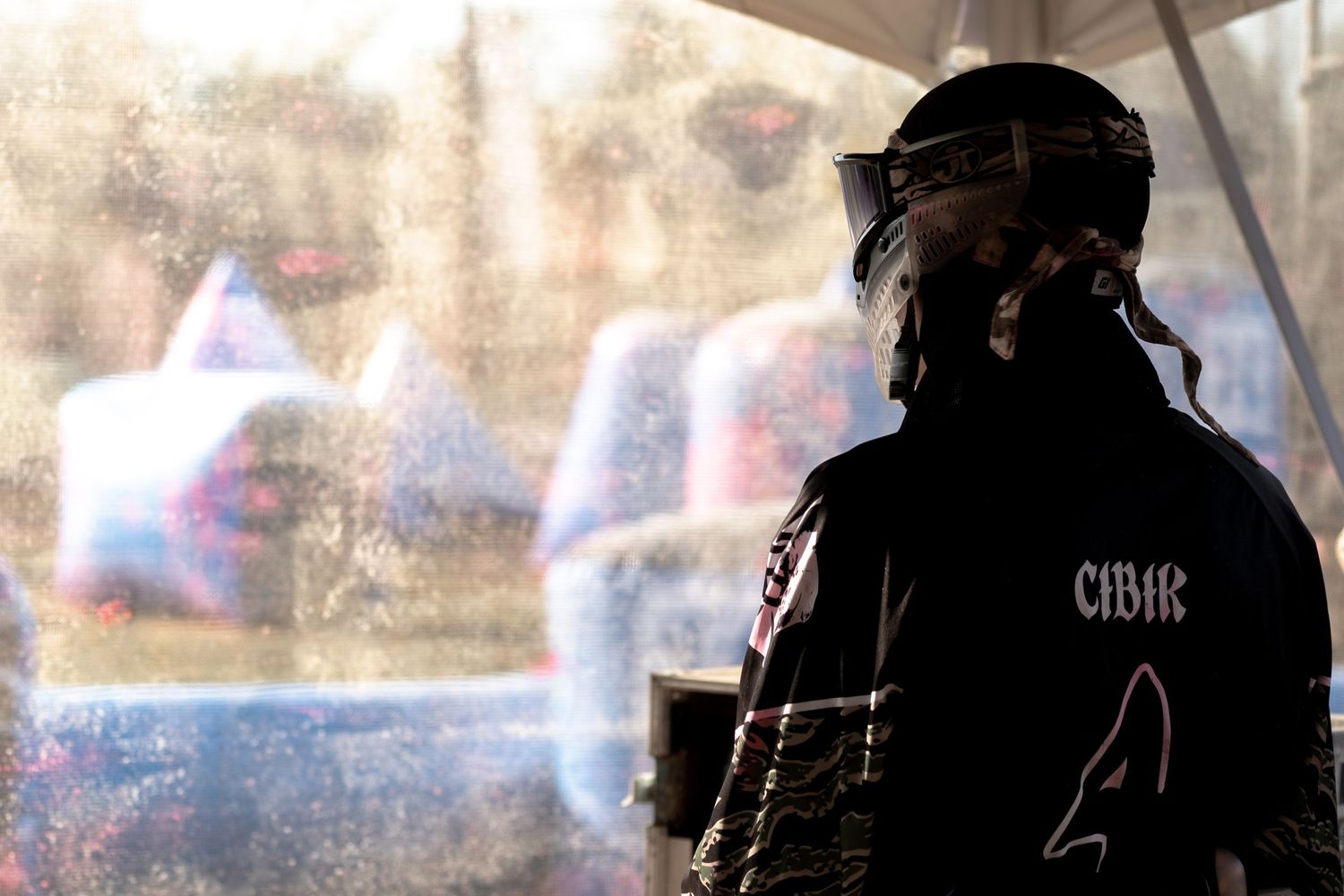 A silhouetted figure in black jacket labeled CIBIR wearing a helmet stands before a blurred colorful background.