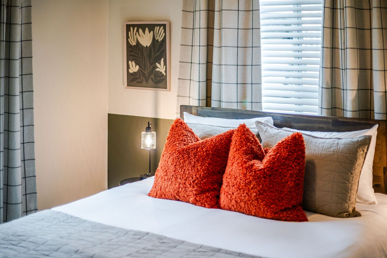 Contemporary bedroom featuring orange throw pillows, white bedding, and window treatments.