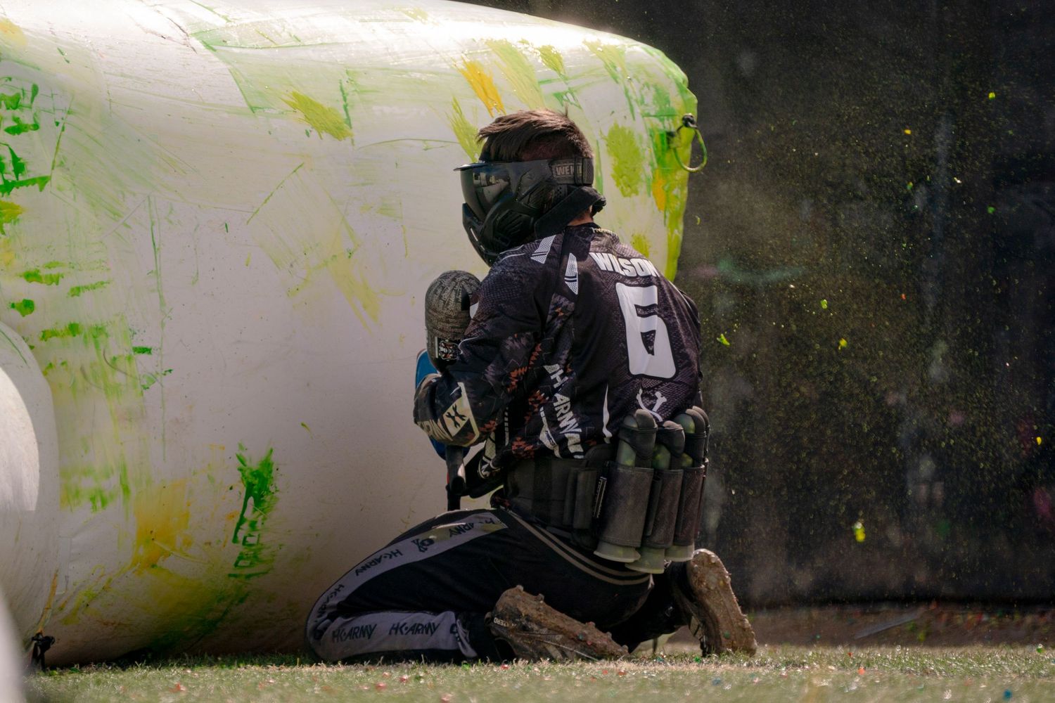 Player takes defensive position behind white inflatable bunker during paintball match.