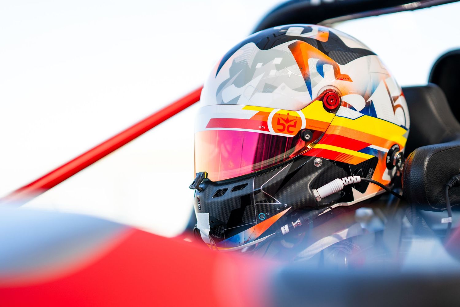 Close-up of racing helmet with red visor inside cockpit of race car.
