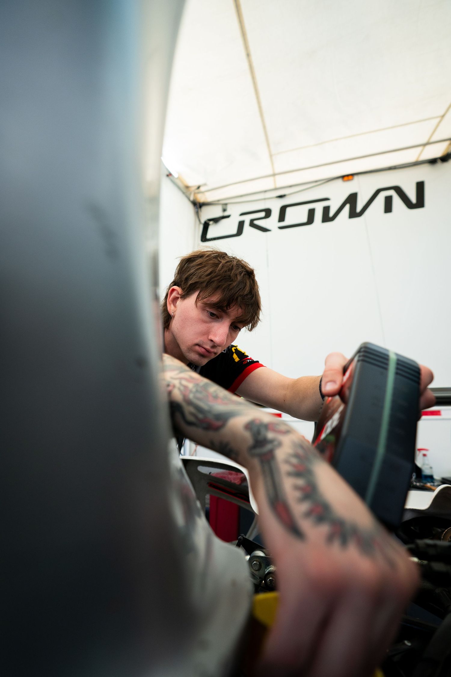 Racing technician working on equipment under a white Crown-branded tent.