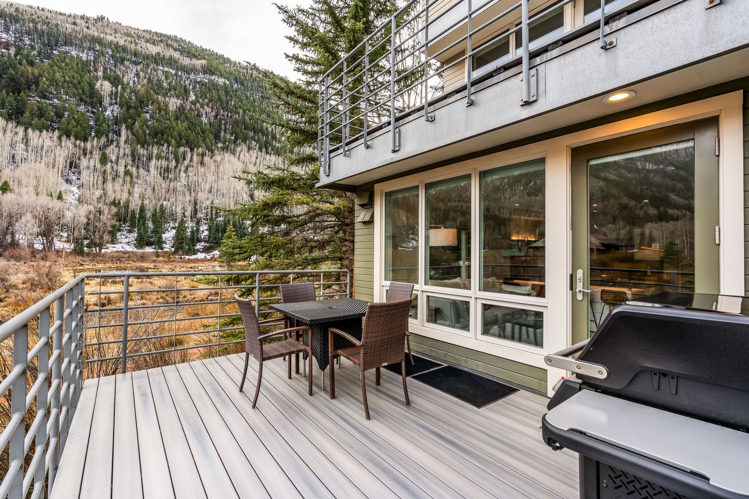 A spacious deck with outdoor dining set and BBQ grill overlooking a forested mountain landscape.