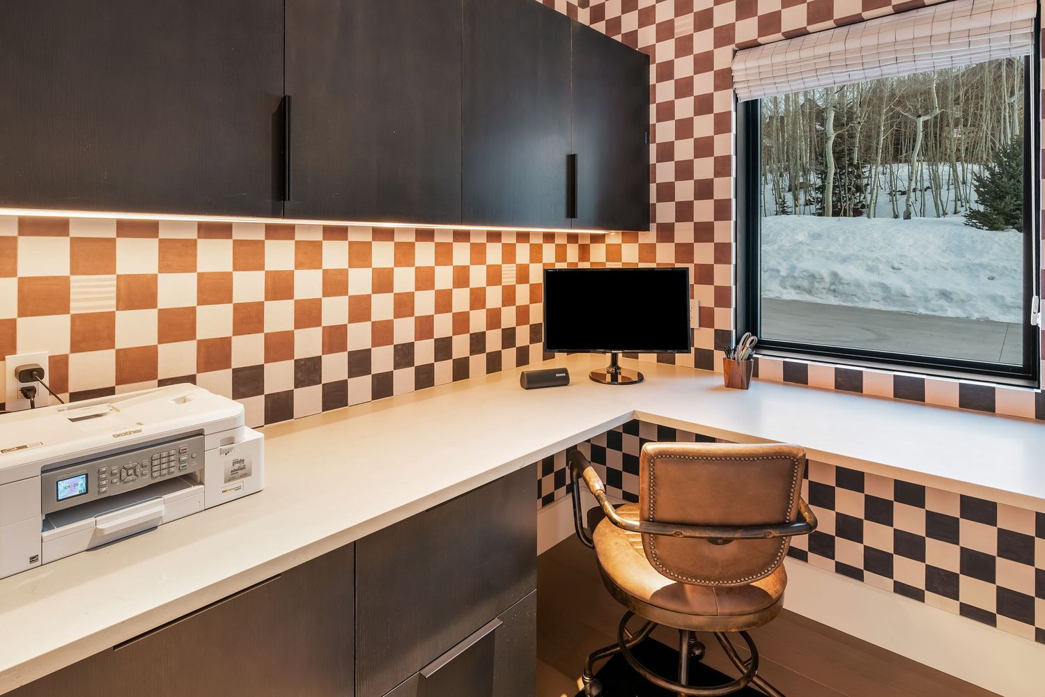 Contemporary office space with checkered wall pattern and built-in desk overlooking snowy landscape.