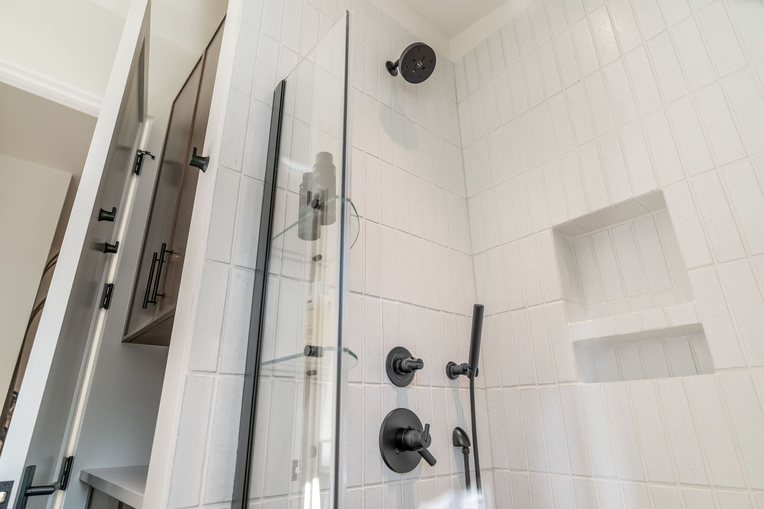 Contemporary white tiled shower with black fixtures and built-in storage niches.