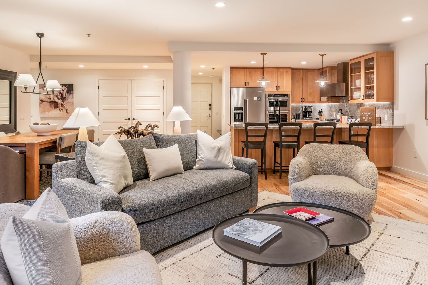 Open-concept living room with gray sofa, accent chairs, and a view into a modern kitchen with stainless steel appliances.