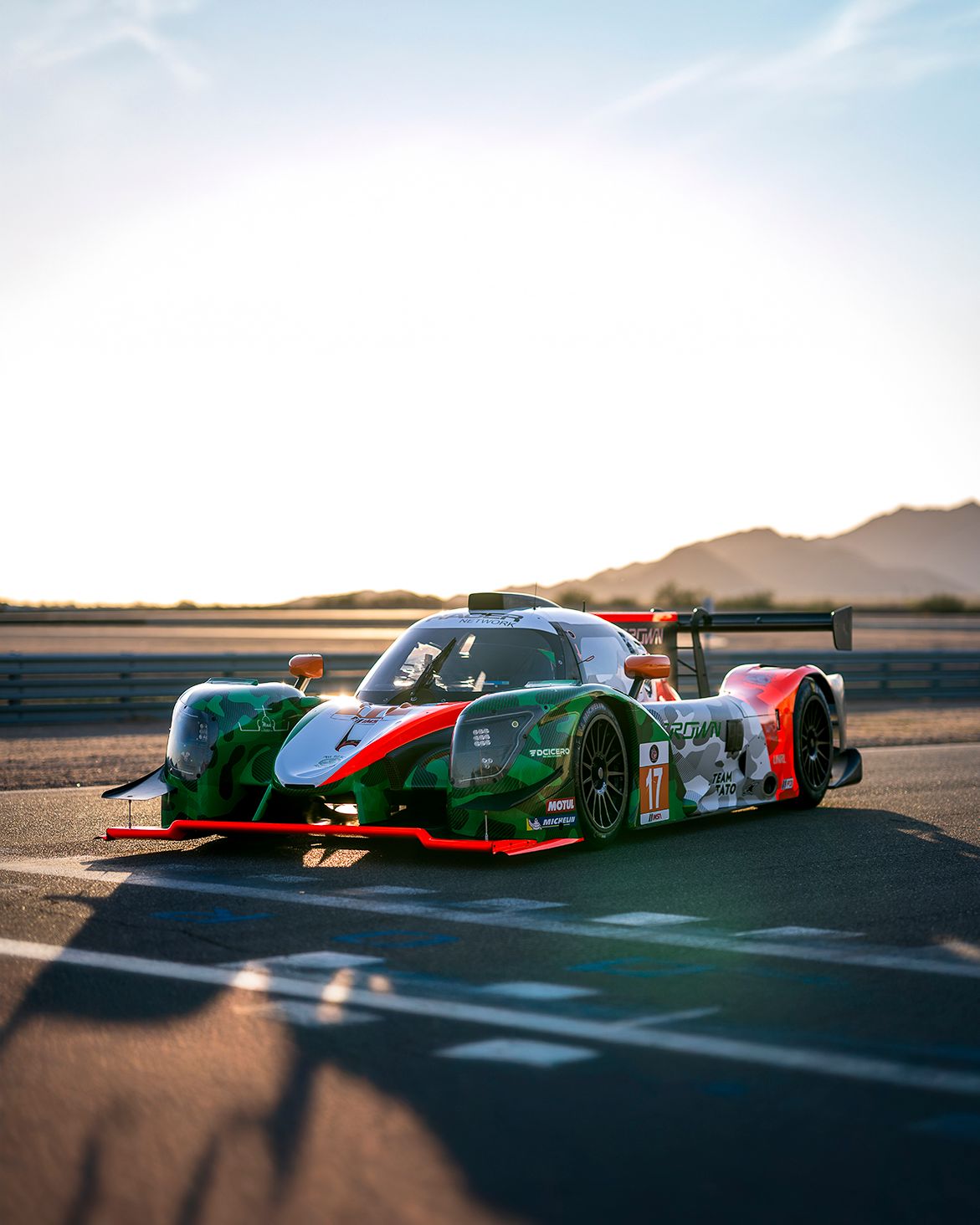 Racing prototype cars lined up on a desert track during a motorsport event.