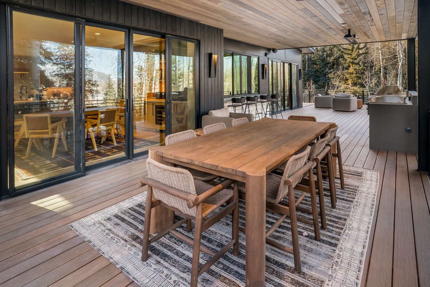 Spacious deck with wooden dining furniture and glass walls overlooking a scenic mountain landscape.