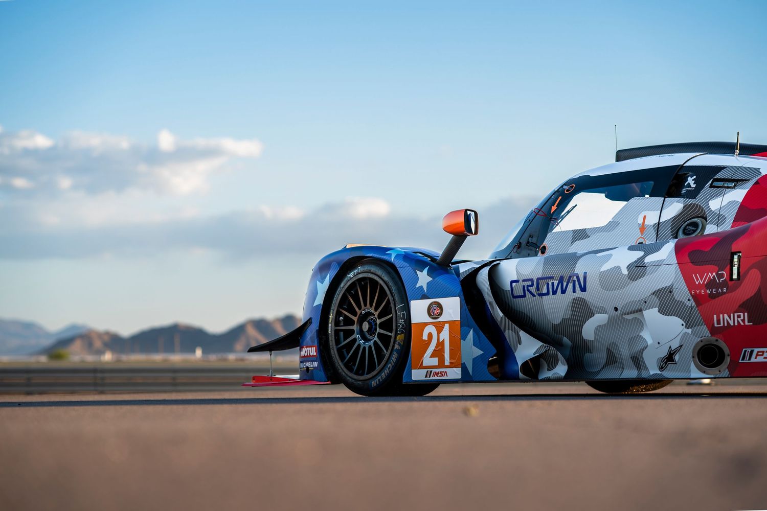 Side profile views of prototype racing cars on desert track under blue sky.