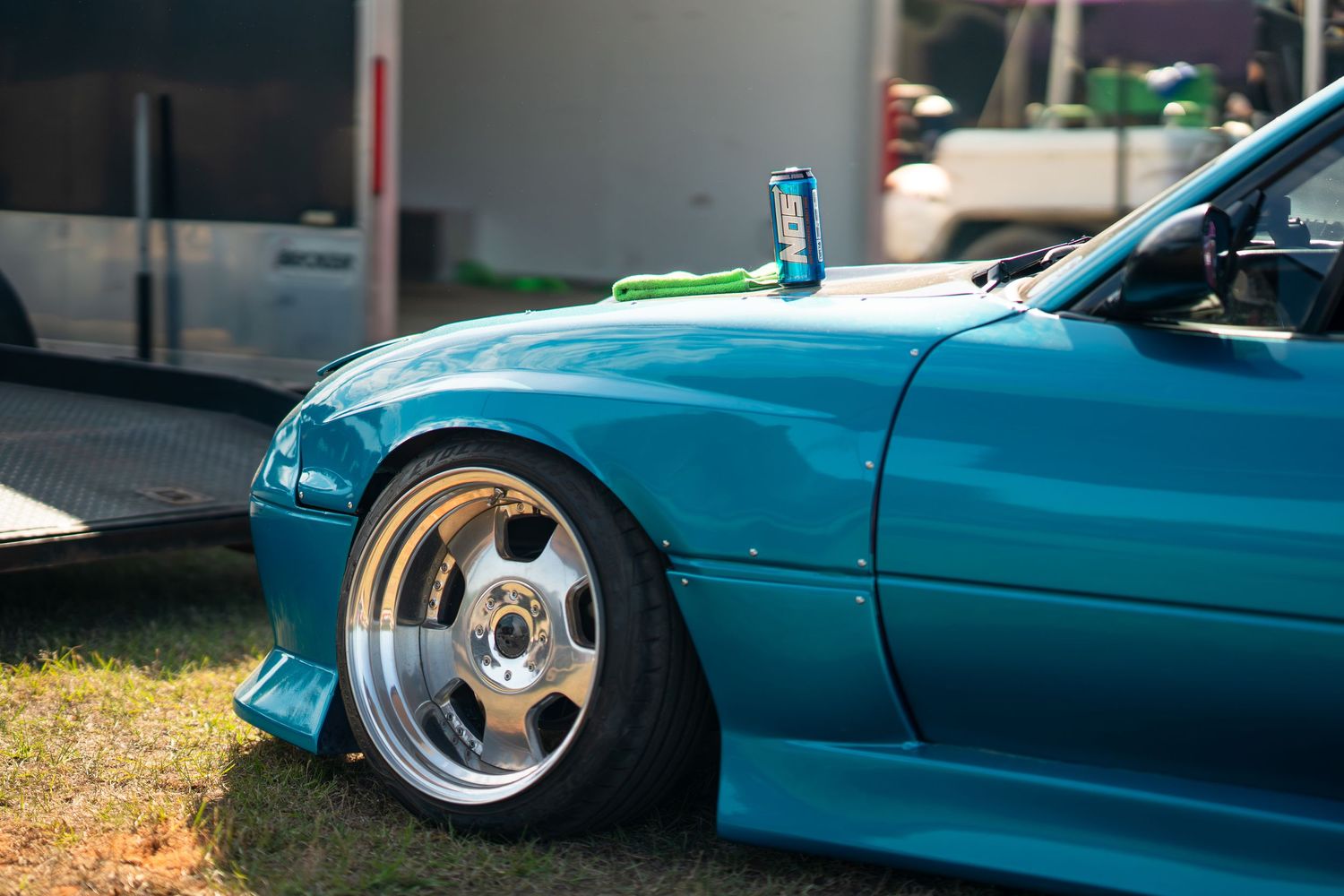 A lowered teal custom car with polished multi-spoke wheels parked on grass at a car show.