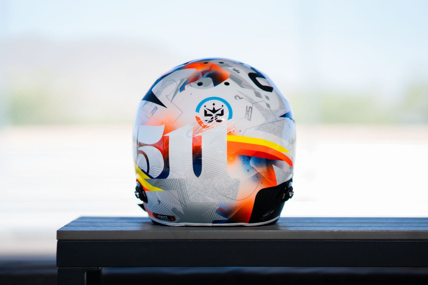 White and orange sports helmet with protective padding sits on a dark surface against a blurred background.