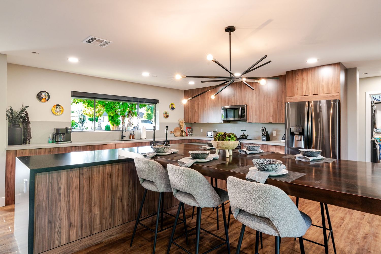Contemporary kitchen featuring wood cabinets, stainless appliances, and white bar stools at a large island counter.