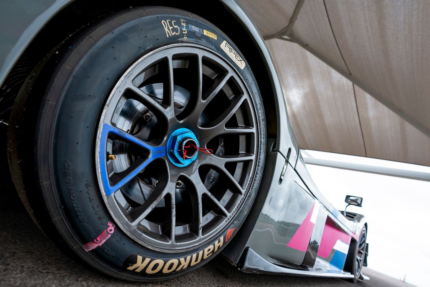 Black racing wheels with performance tires mounted on a race car featuring pink and blue accents.