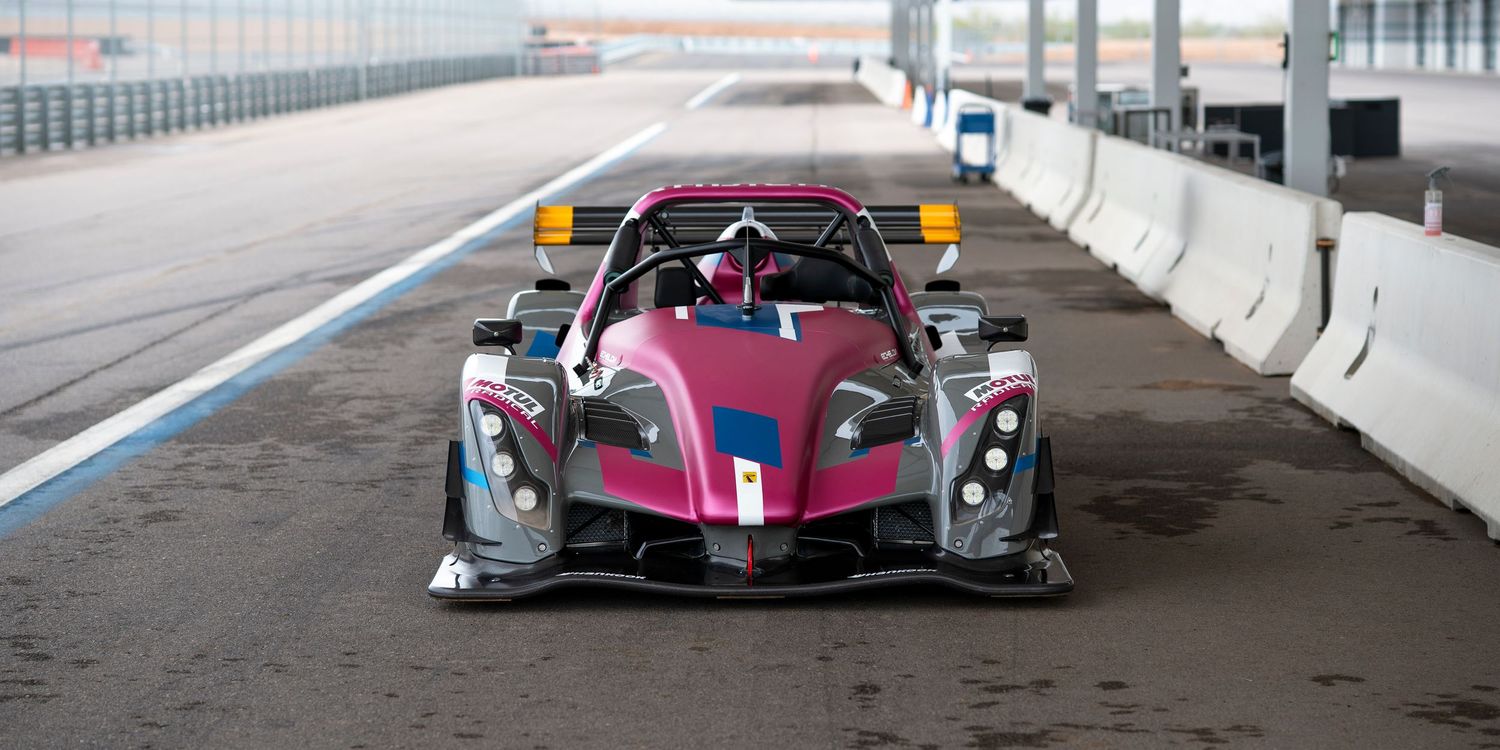 A sleek purple and black prototype racing car with aerodynamic bodywork parked on a racetrack.