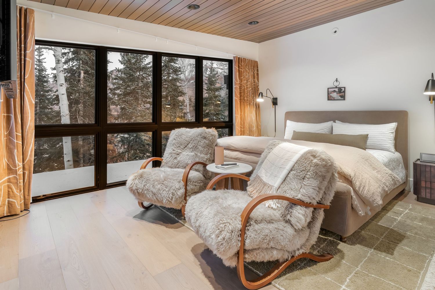 Modern mountain cabin bedroom with wood ceiling, panoramic windows, and cozy neutral decor.