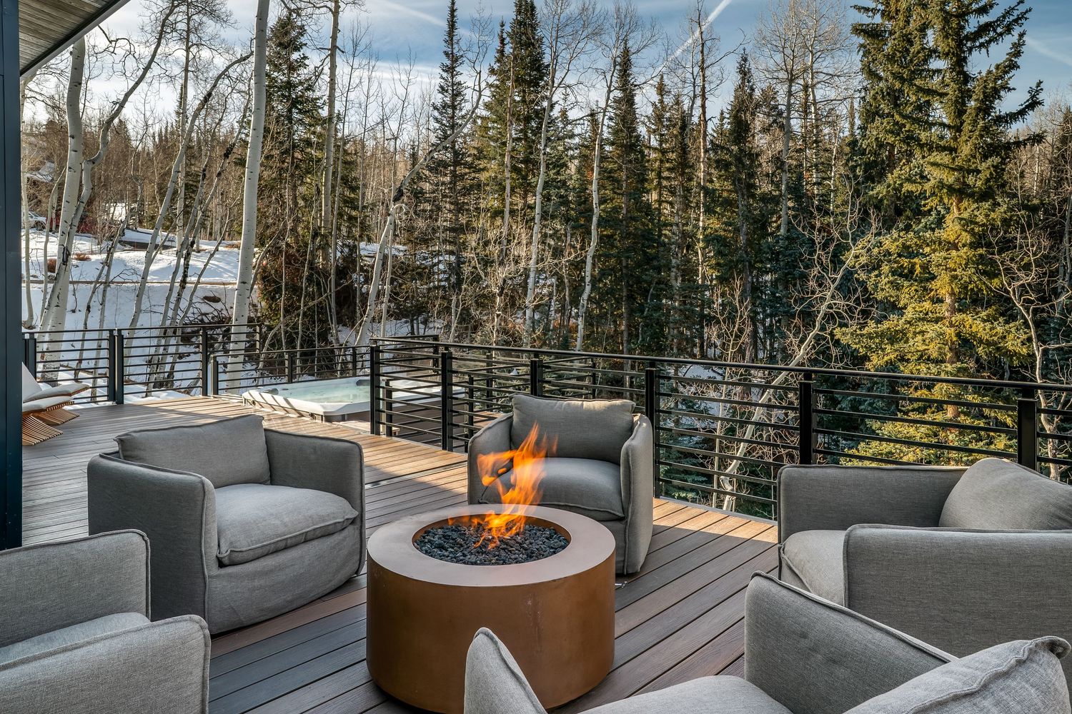 Outdoor lounge area with modern grey seating and fire pit offering panoramic mountain and forest views.