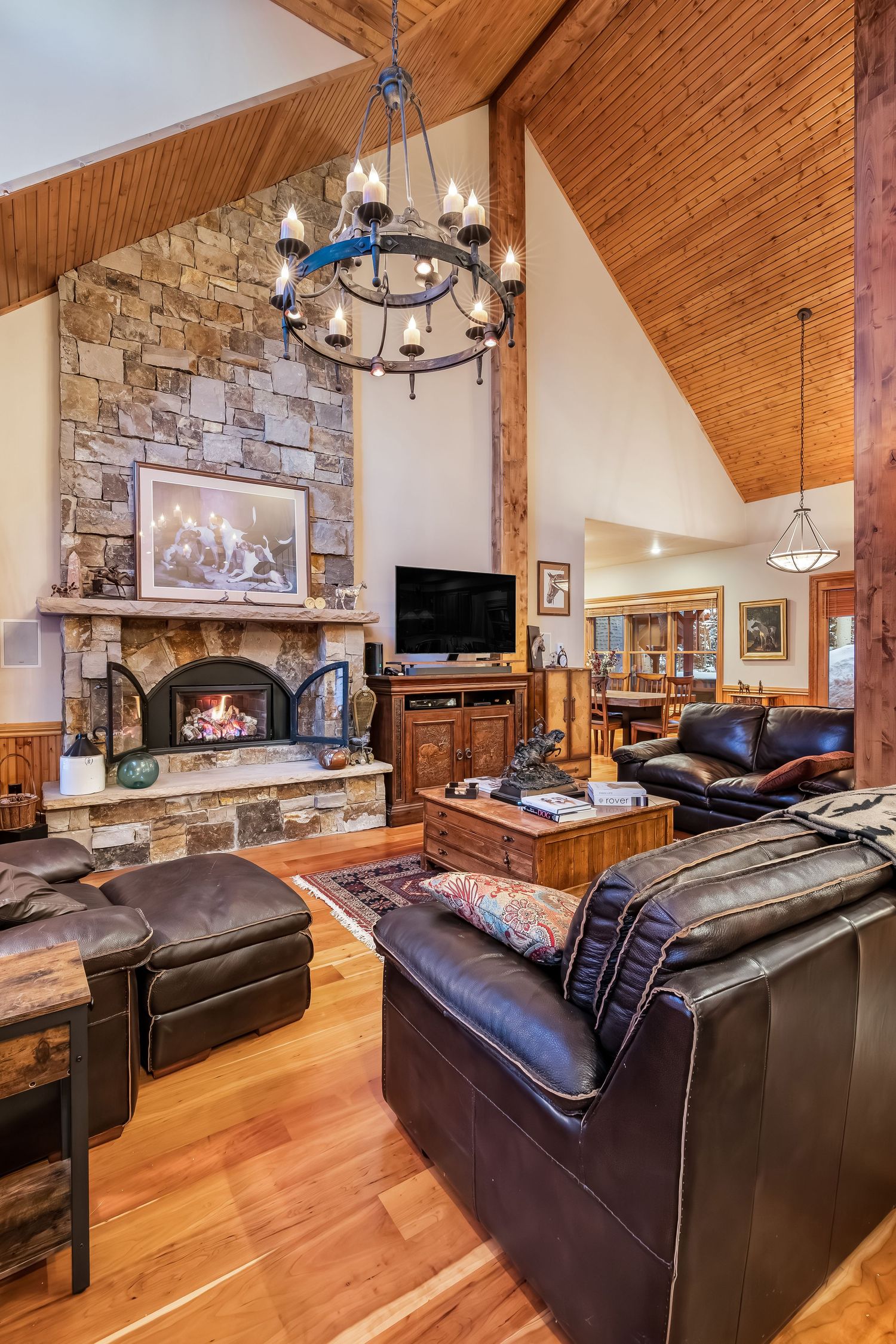 Rustic mountain lodge living room with stone fireplace, wood beam ceiling, and leather sectional sofa.