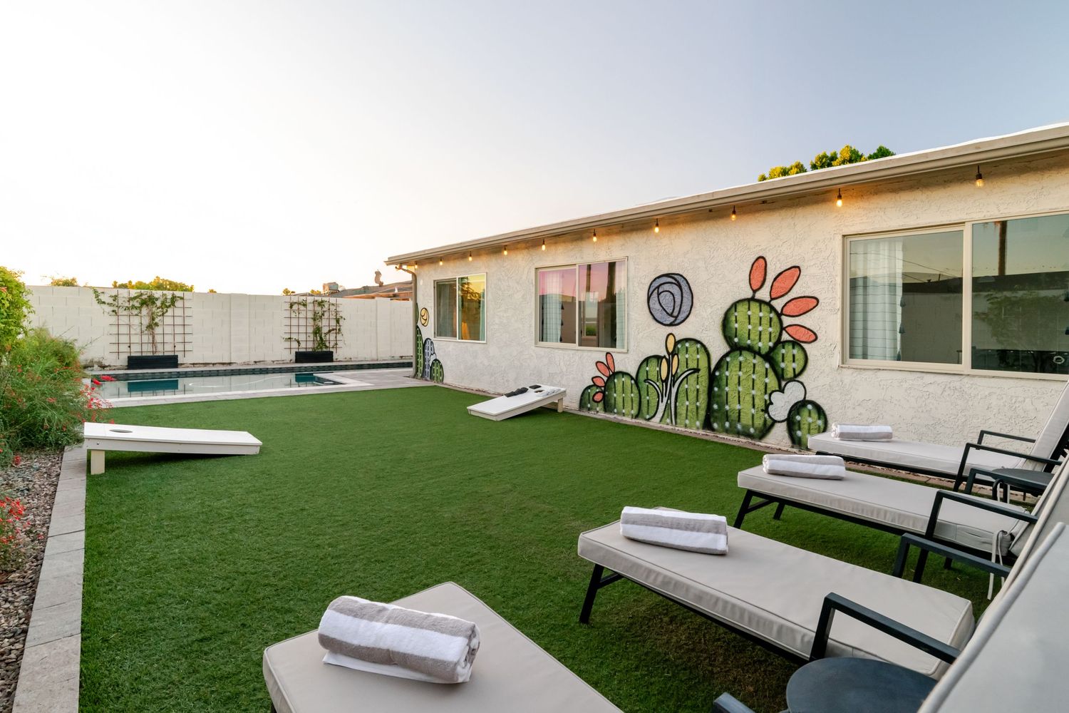 Outdoor patio space with artificial turf, lounge chairs, and white cushions surrounded by a modern building exterior.