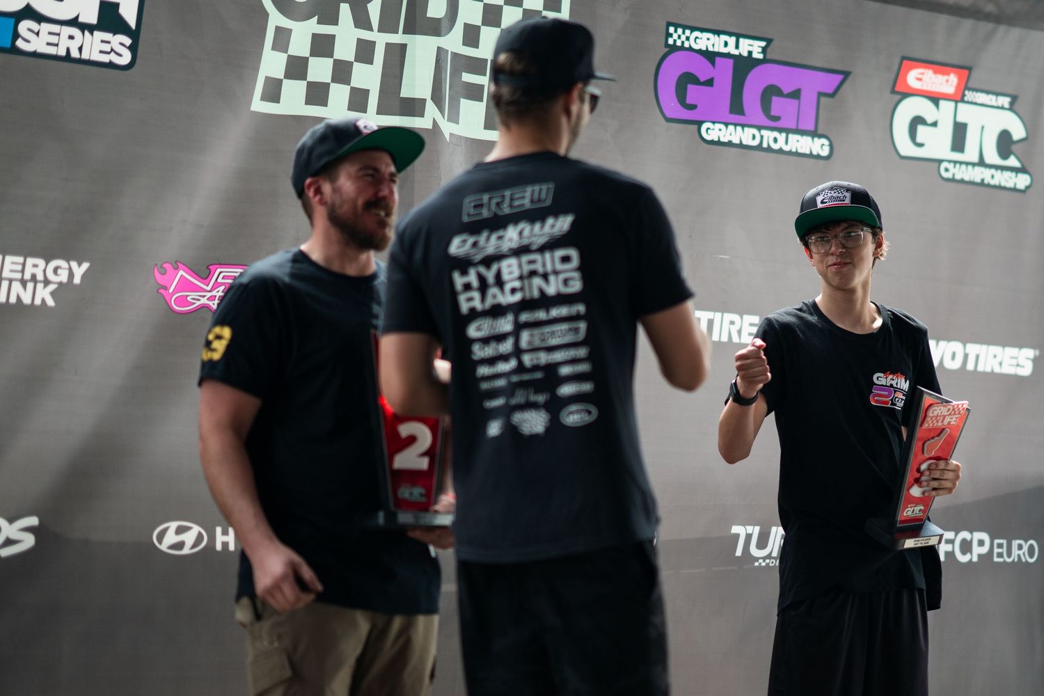 Three people conversing at Grid Life motorsport event in front of branded backdrop.