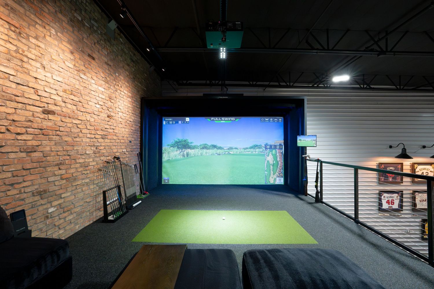 Golf simulator setup in spacious garage area with exposed brick walls and projector screen.