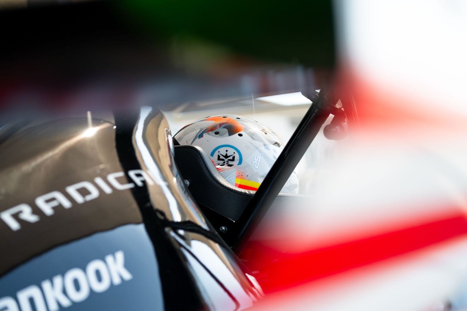 Close-up detail of Radical race car showing partial helmet view through windscreen.