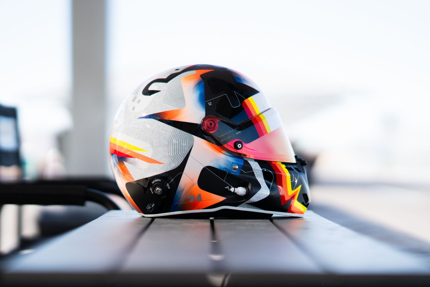 Racing helmet with vibrant orange, black and white design sits on reflective surface in studio lighting.