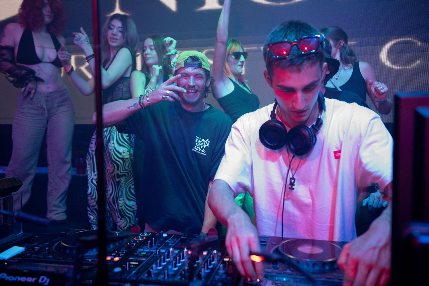 DJ performs at a nightclub using professional equipment under blue and purple lighting.