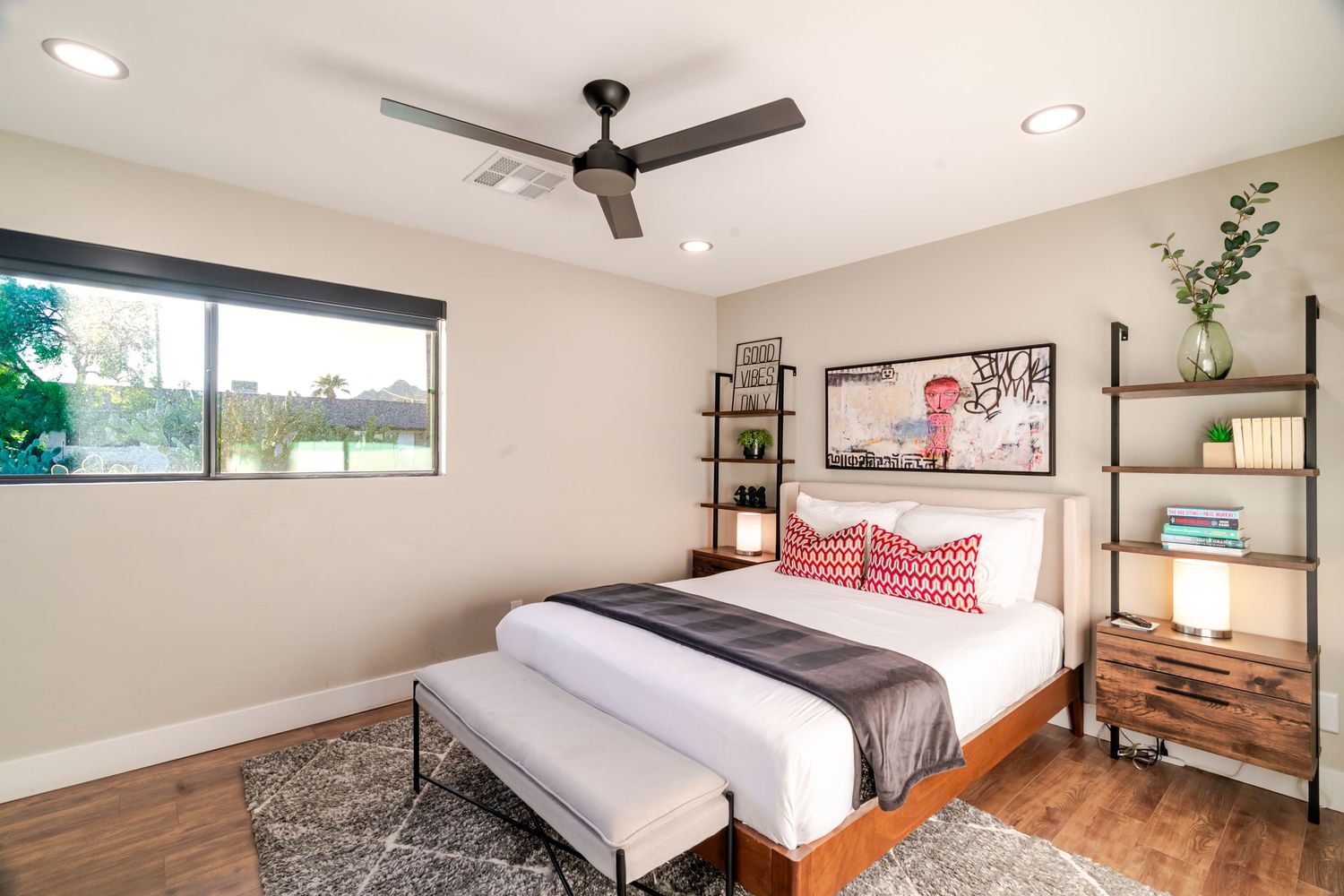 Contemporary bedroom with wooden furniture, gray bedding, and decorative red pillows under a modern ceiling fan.
