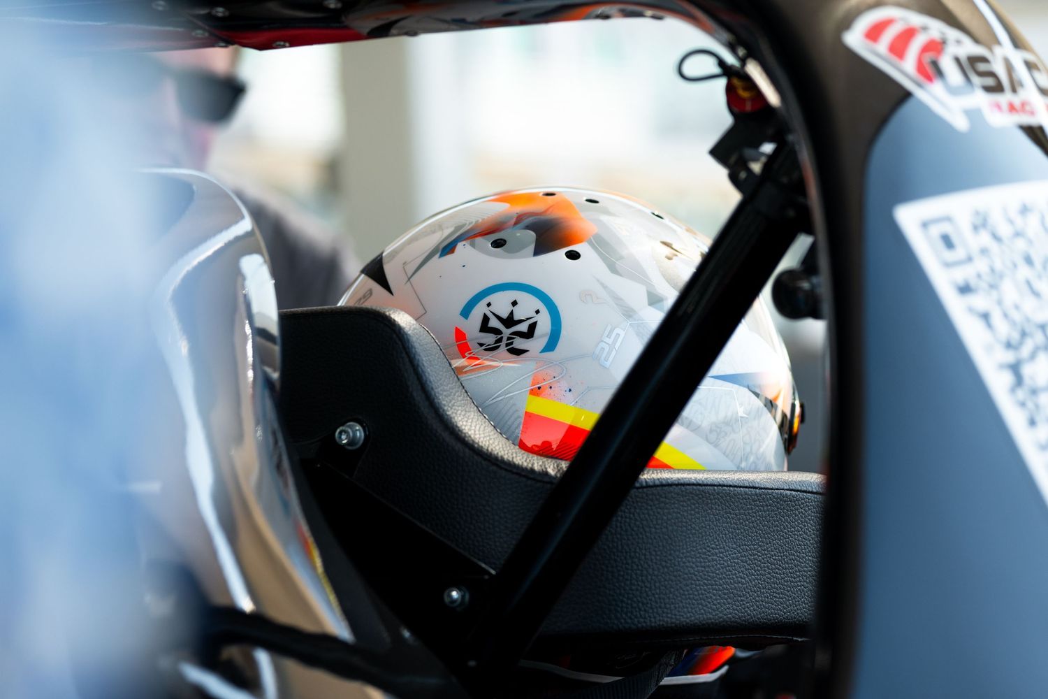 Racing helmets and safety equipment visible through blurred glass or window.