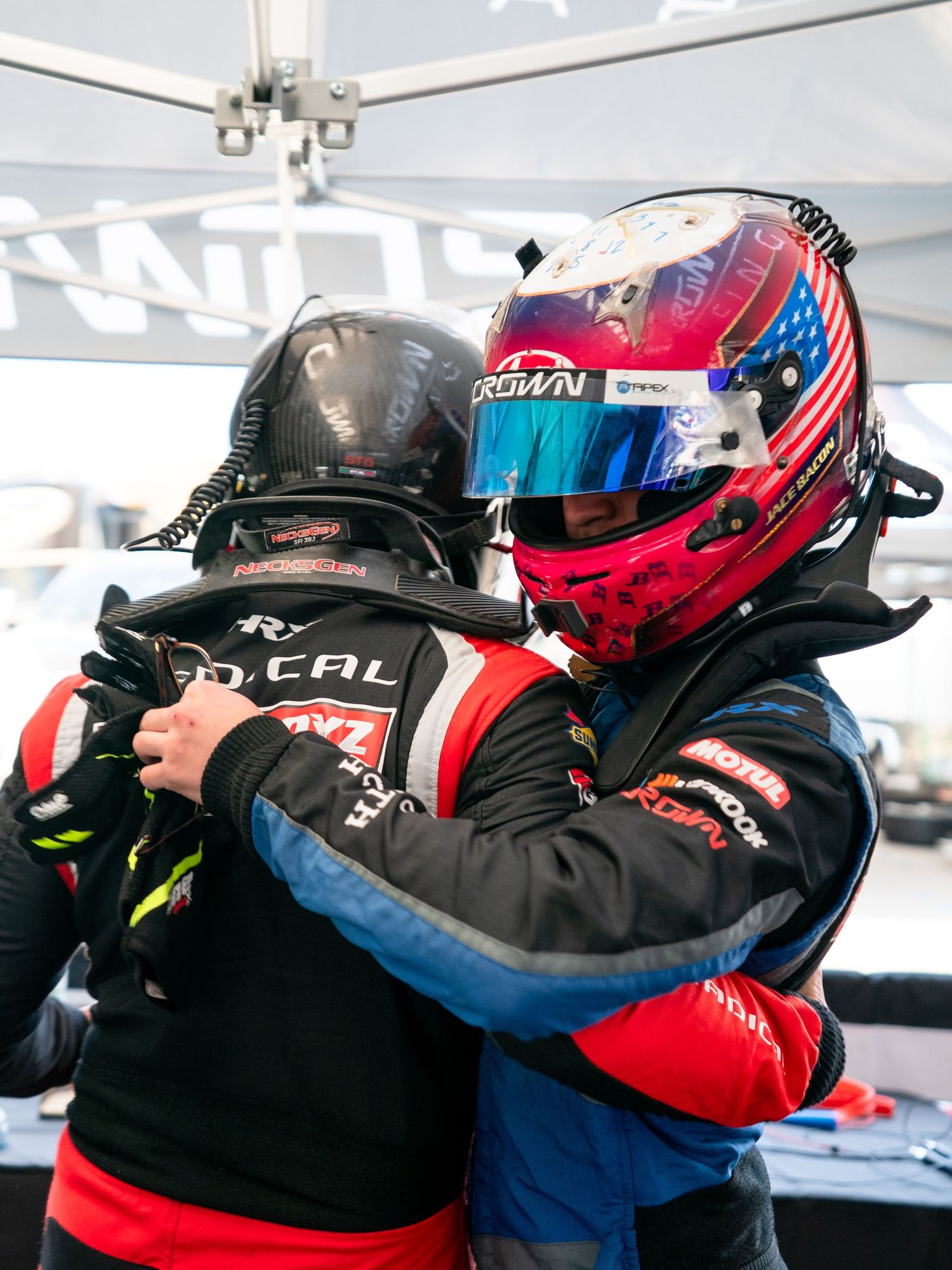 Racing team members celebrating with victory hugs and helmets after successful race.