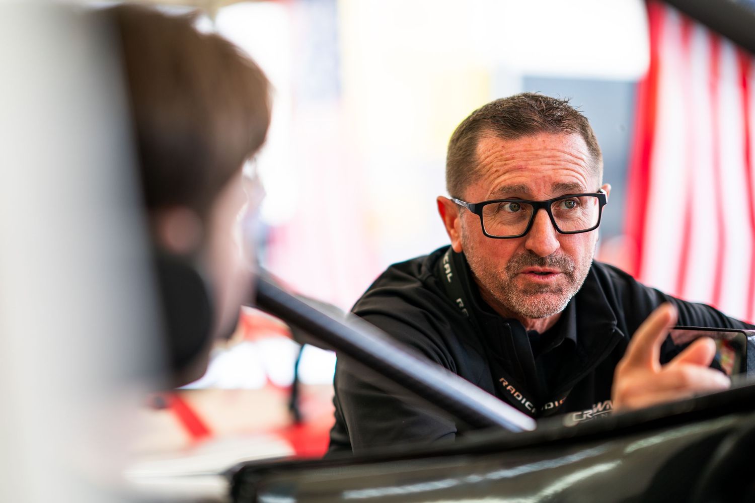 Racing team members discussing strategy in the pit garage during event preparation.