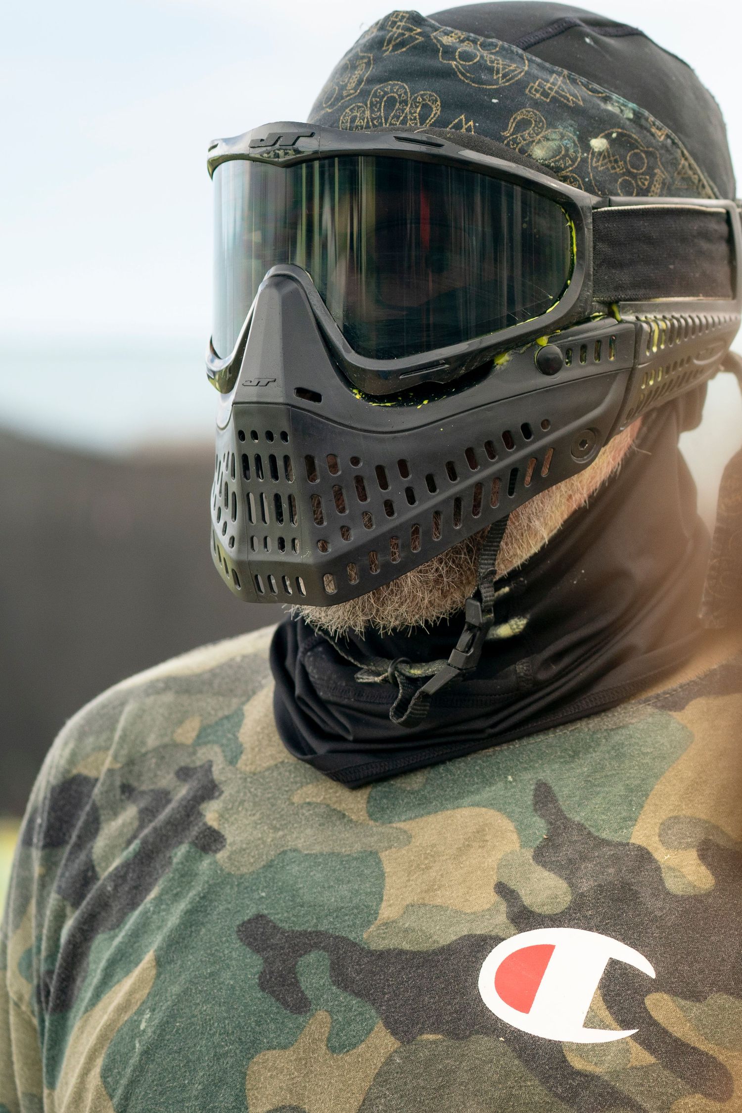Player wearing camouflage clothing and protective paintball mask with goggles.