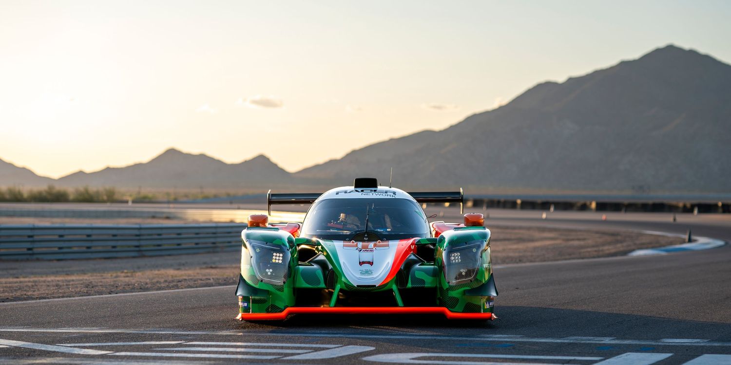 Silhouettes of race cars against mountain backdrop during sunset on desert racing circuit.