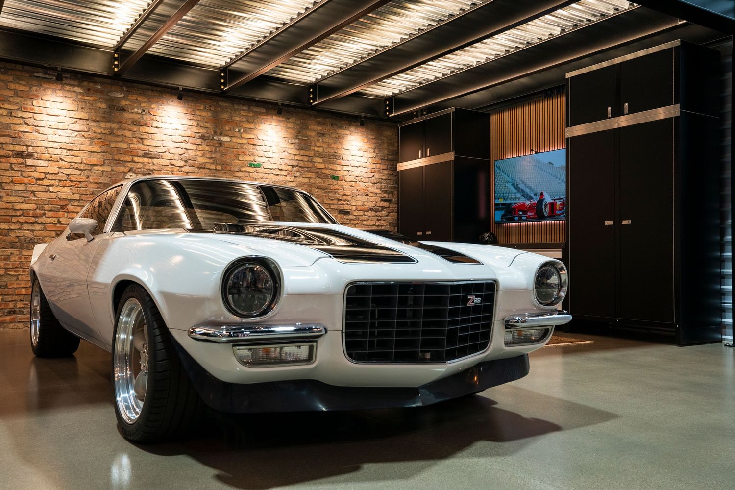 Vintage white sports car displayed in luxury garage space with brick walls and ambient lighting.