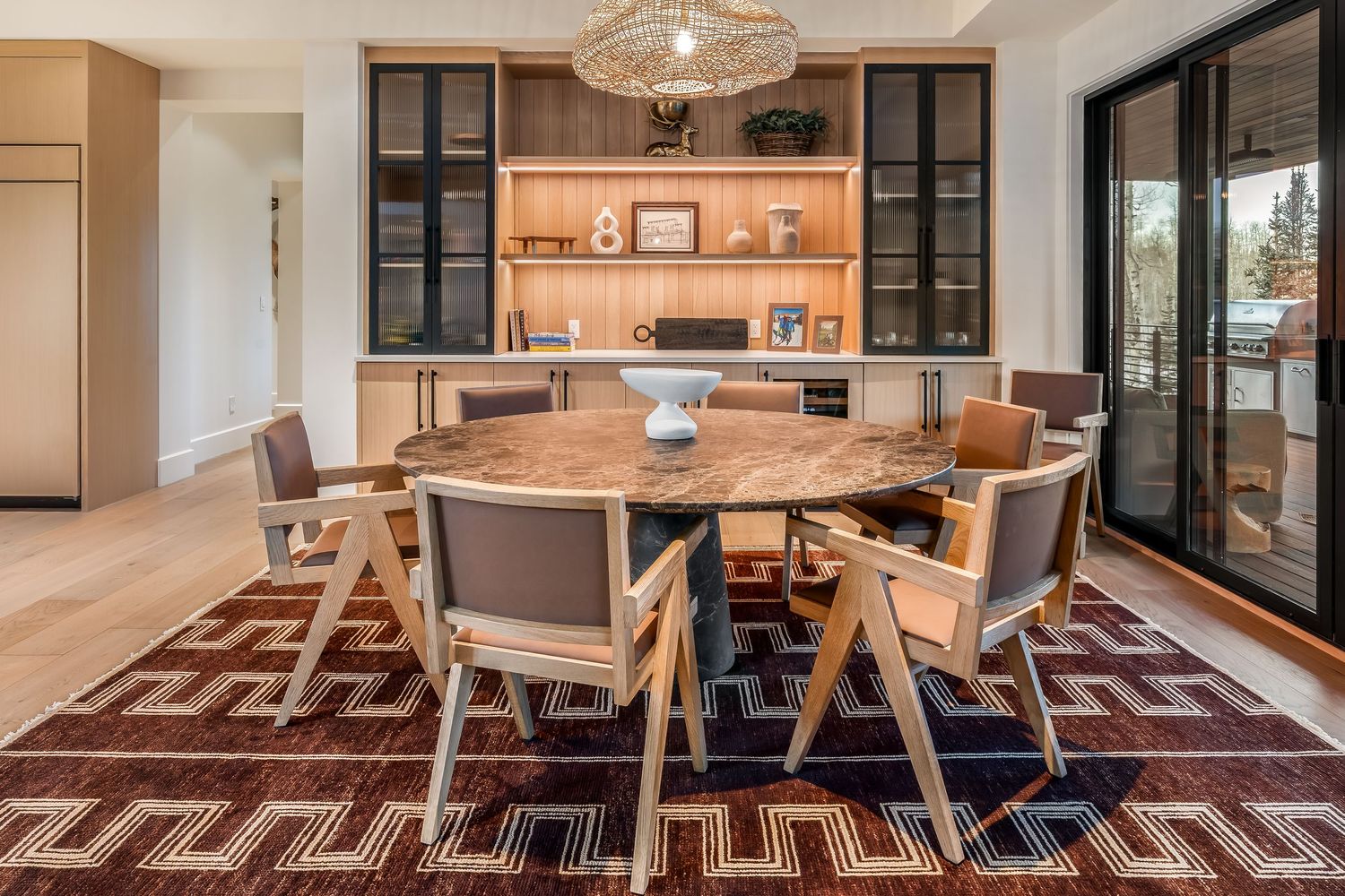 Dining area with wooden table and pendant lighting showcases panoramic forest views through large windows.