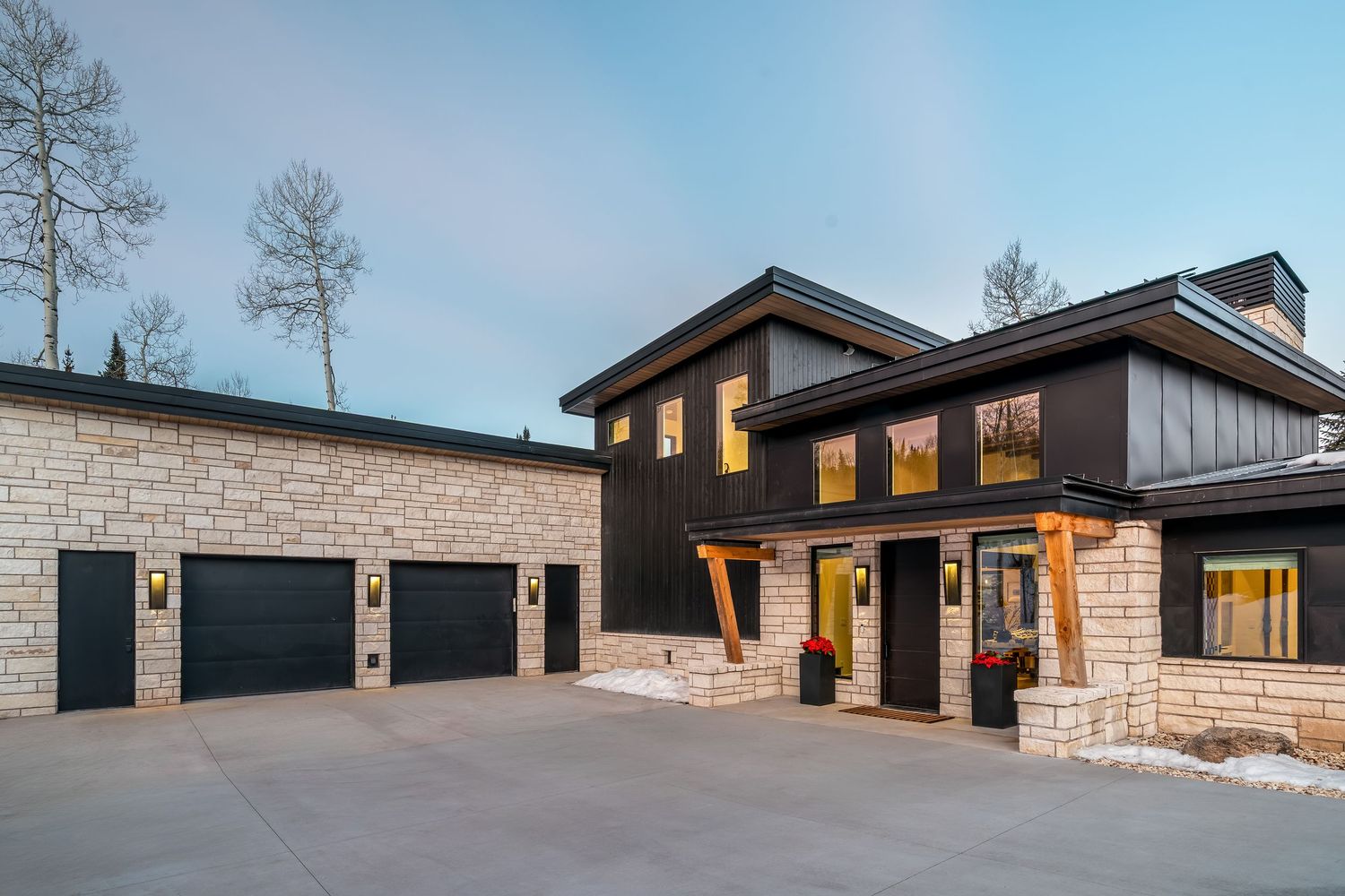 Modern farmhouse-style buildings with dark metal roofs and stone accents line up along a snowy landscape at dusk.
