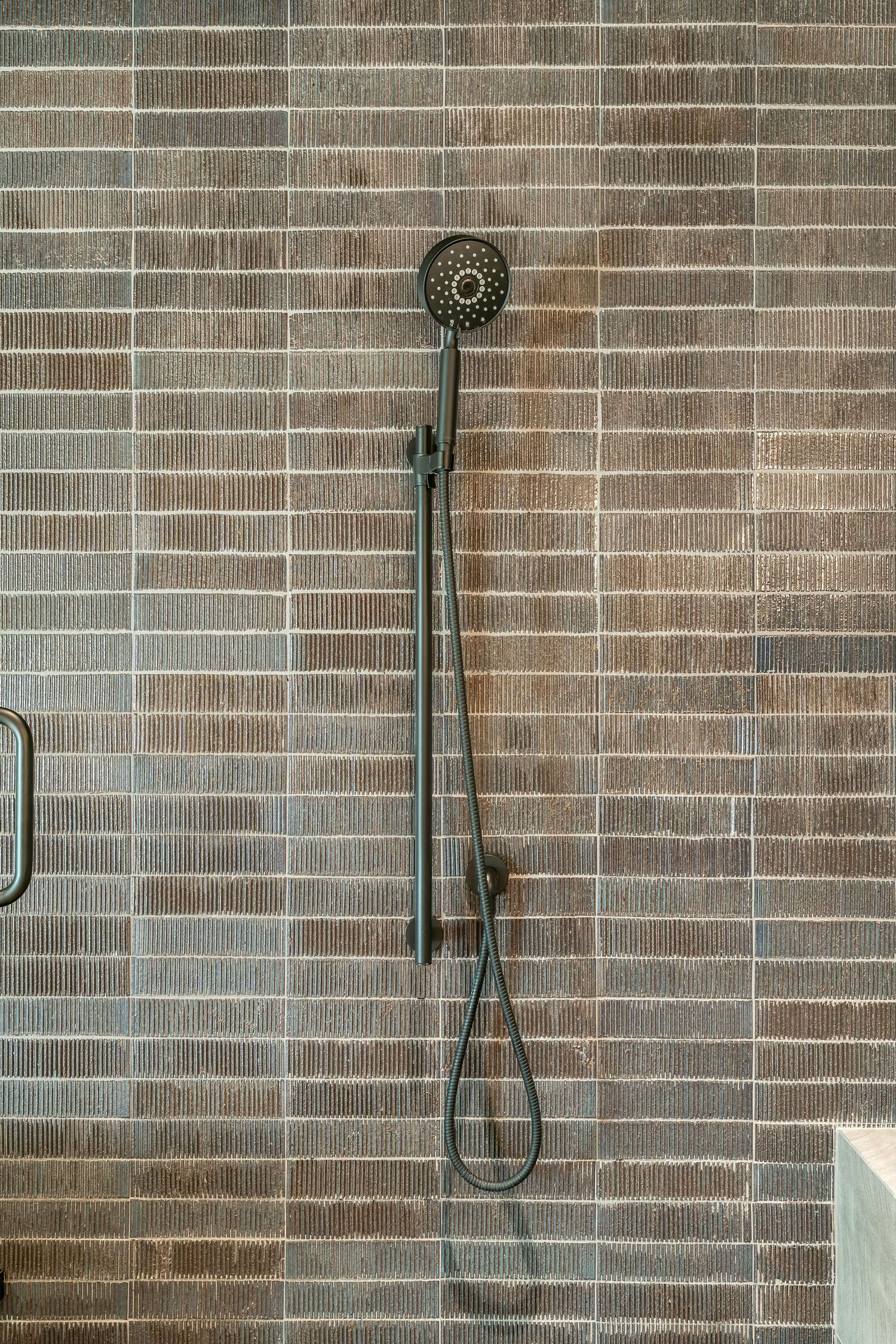 Contemporary bathroom wall featuring sleek black shower fixtures mounted on textured brown tile backsplash.