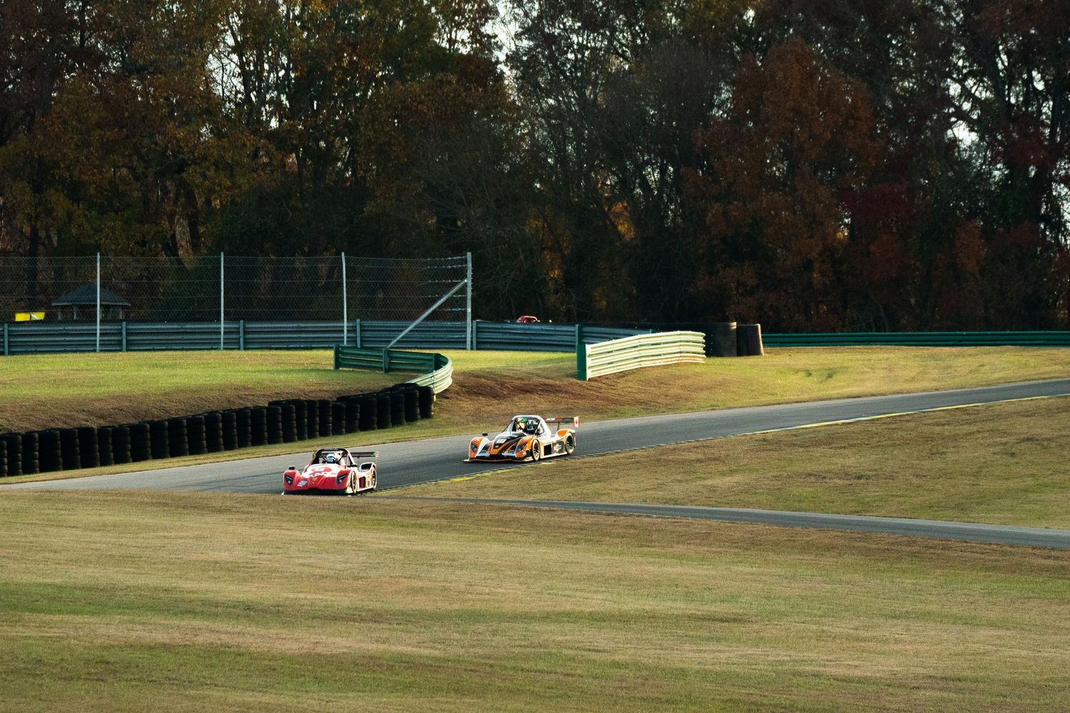 Race cars competing on a scenic race track surrounded by autumn trees.