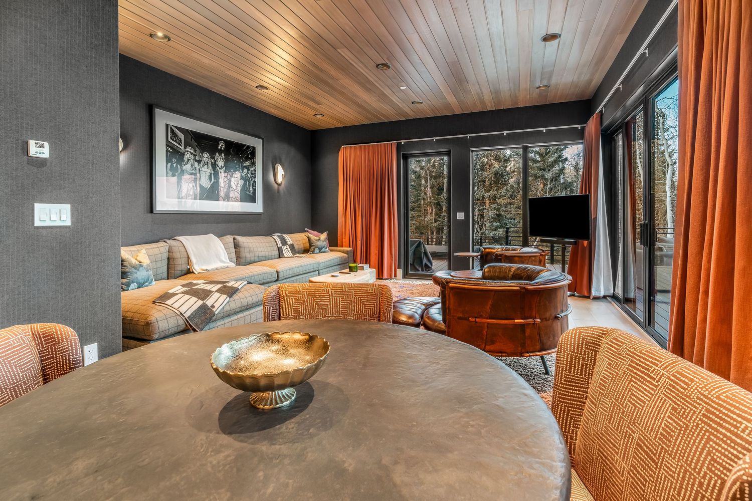 Modern living area with wood ceiling, orange curtains, and comfortable seating arrangements.