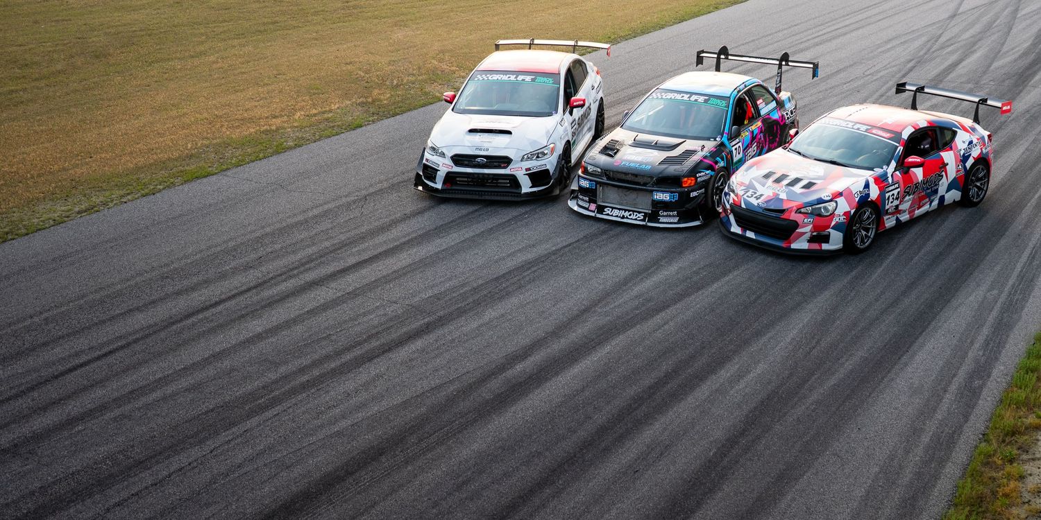 Three racing cars, including a Subaru WRX and Toyota GT86, compete on a race track during a motorsport event.