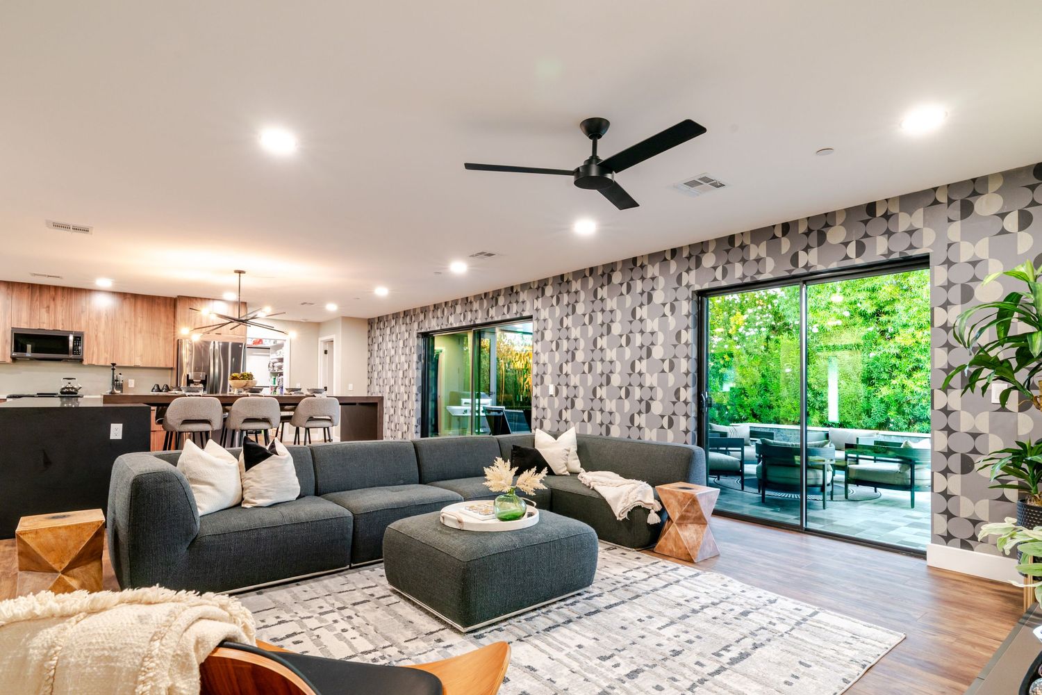 Modern living room with gray sectional sofa, patterned wallpaper, and sliding glass doors leading to outdoor patio.